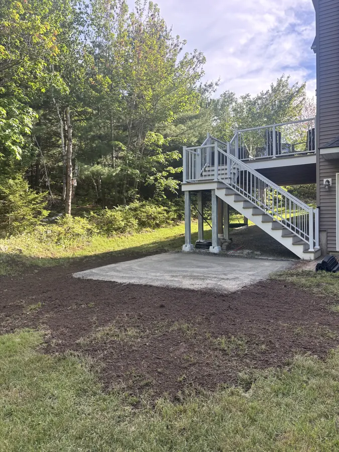 Freshly graded backyard soil and a concrete pad below an elevated deck with white stairs — landscaping project in Halifax, Nova Scotia