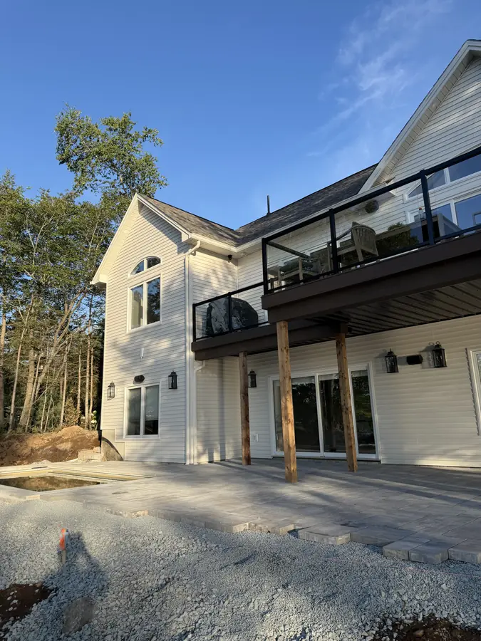 Large two-storey home with a glass-railed deck above a gravel patio base — hardscaping project in Halifax, Nova Scotia