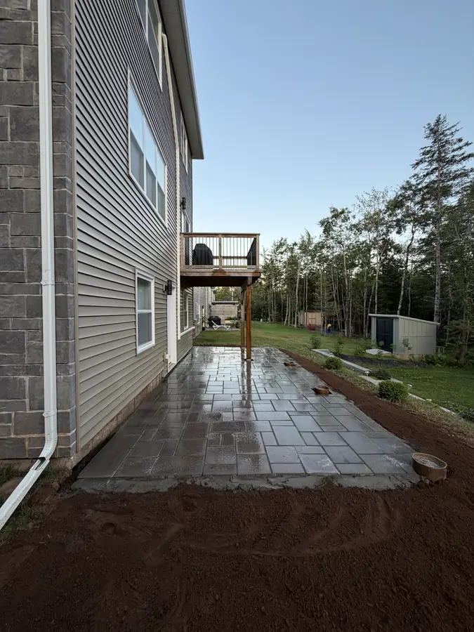 Large-format paver patio freshly laid beside a home with graded soil along the edge — hardscaping project in Halifax, Nova Scotia