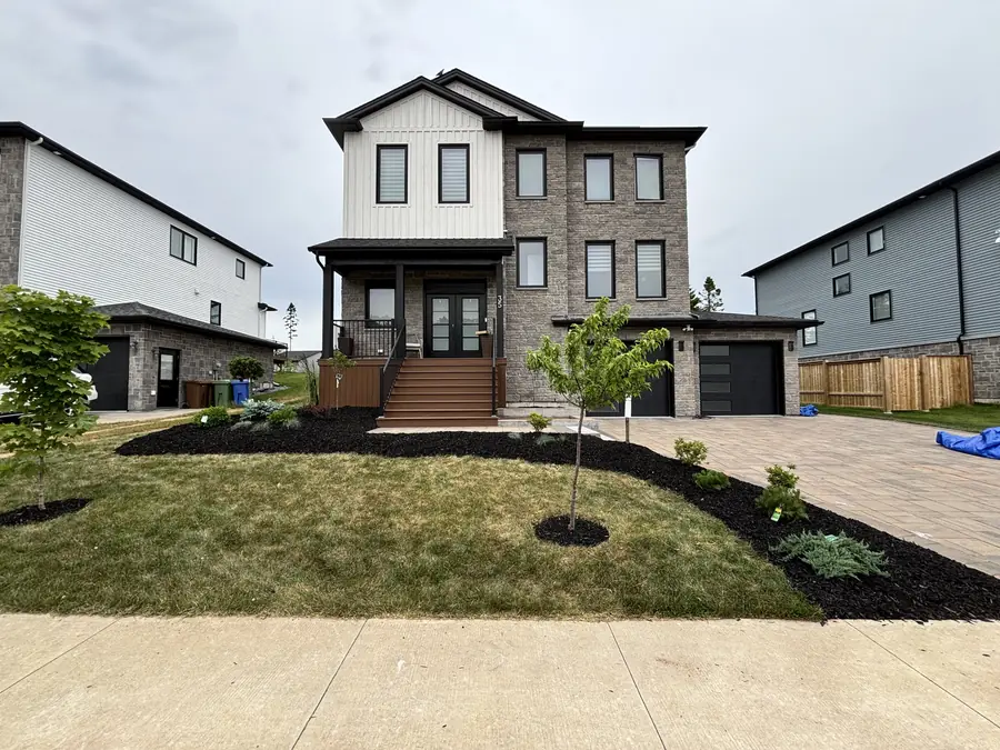 Modern two-storey home with a freshly landscaped front yard, black mulch beds, a young tree and a paver driveway — landscaping project in Halifax, Nova Scotia