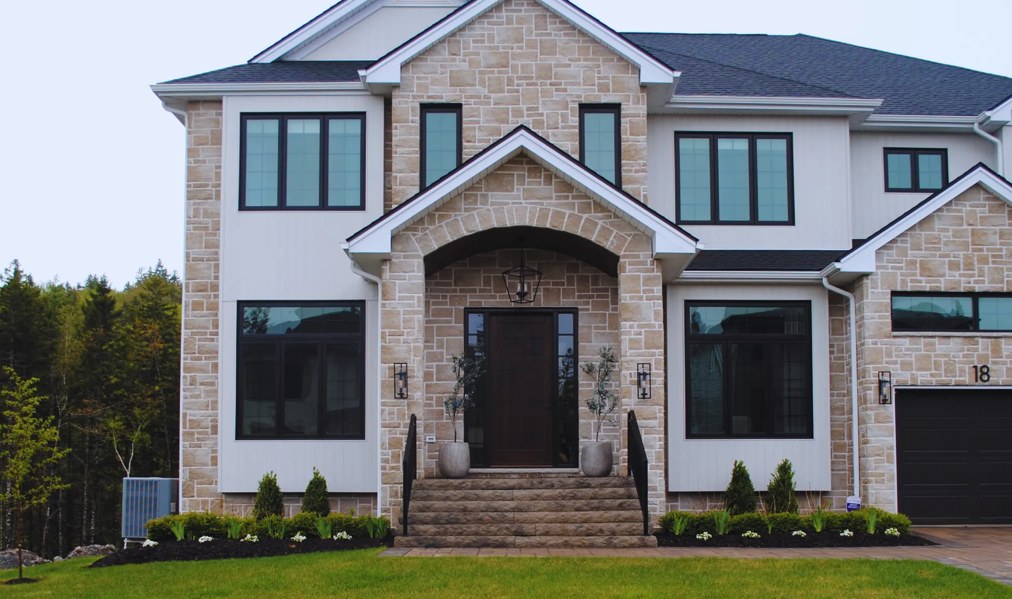 Stone and white-panel home with clean mulched front beds and evergreen shrubs flanking the entrance