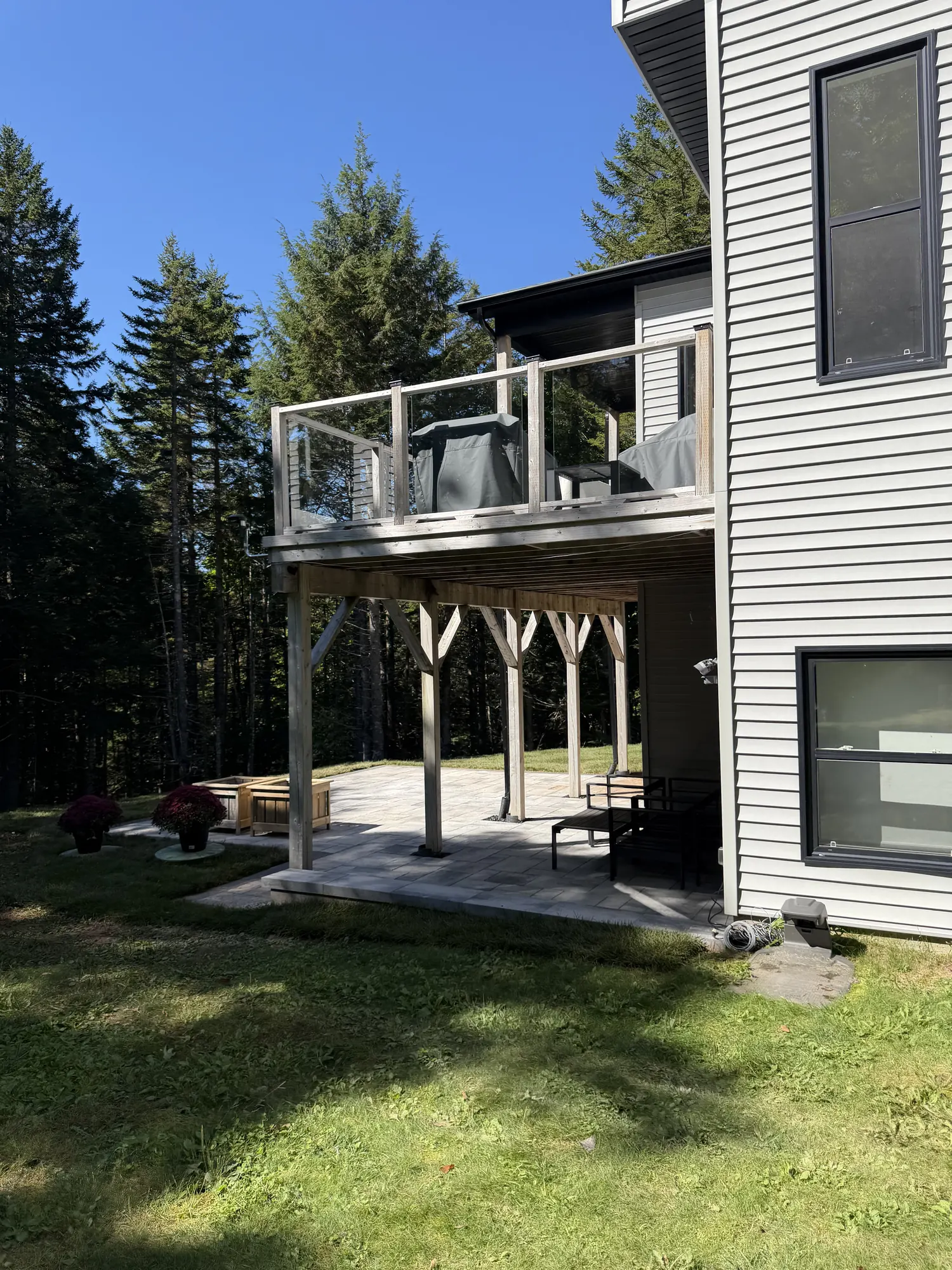 Stone patio and seating area beneath an elevated deck at a modern two-storey home